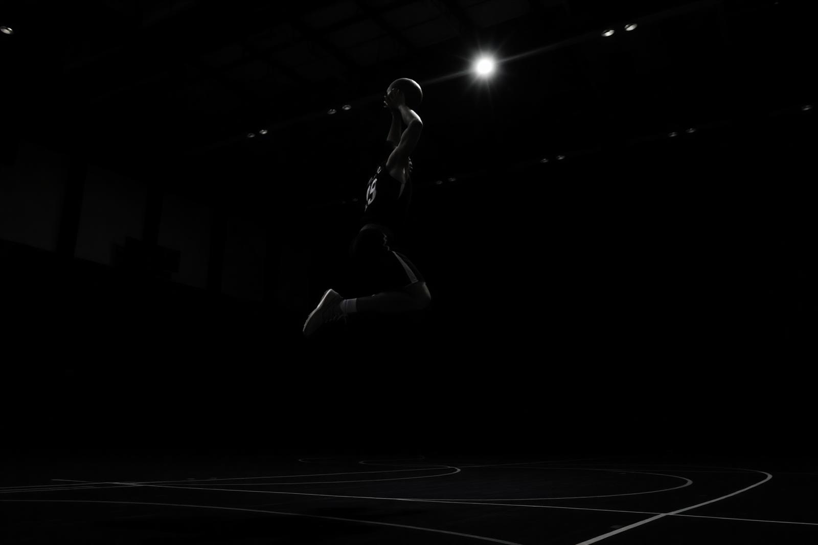 Basketball player mid-air during an explosive jump in a dark gym