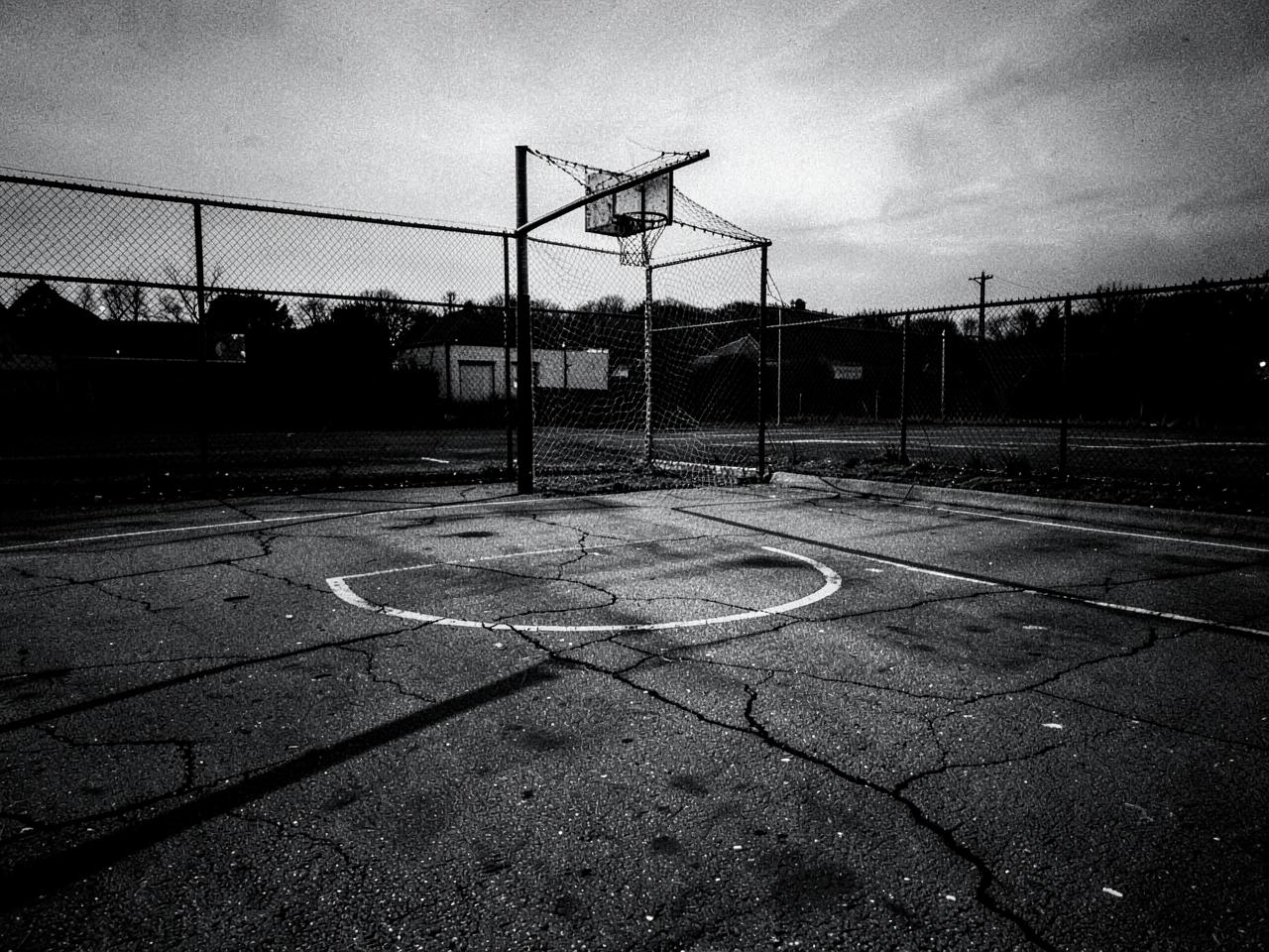 Empty outdoor asphalt basketball court with a chain net at dusk